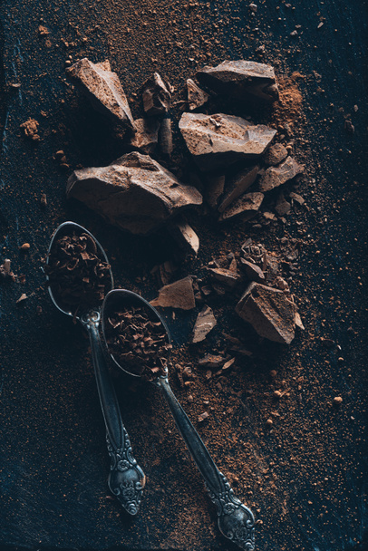 vista superior de cucharas vintage, trozos de chocolate y cacao en polvo en la superficie oscura
  - Foto, imagen