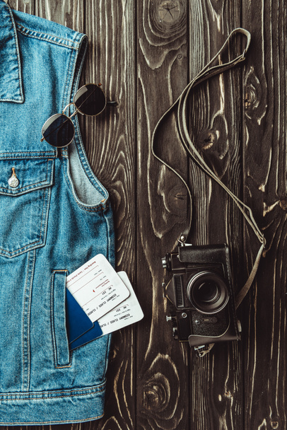 flat lay with denim vest, passports, tickets, sunglasses and retro photo camera on dark wooden surface - Photo, Image