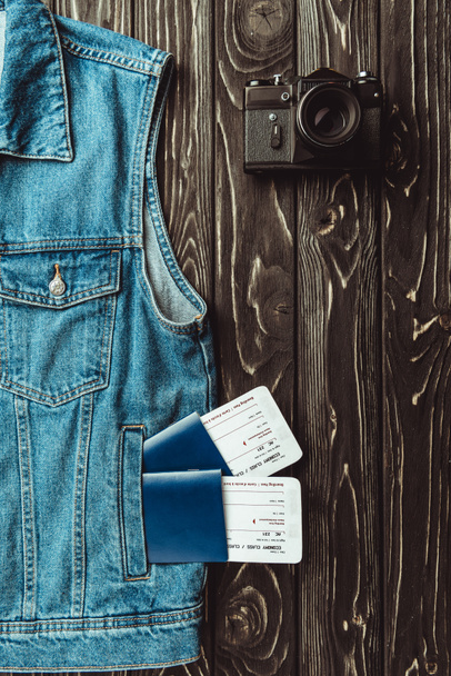 flat lay with denim vest, passports, tickets and retro photo camera on dark wooden surface - Photo, Image