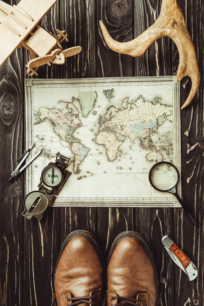 top view of travel setting with map, shoes, compass, magnifying glass and decorative horns on dark wooden surface - Zdjęcie, obraz
