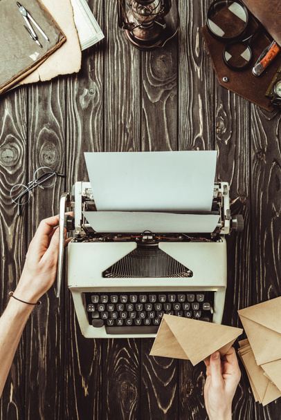 vista parcial de las manos femeninas, máquina de escribir, lupas y sobres en la mesa de madera
 - Foto, Imagen