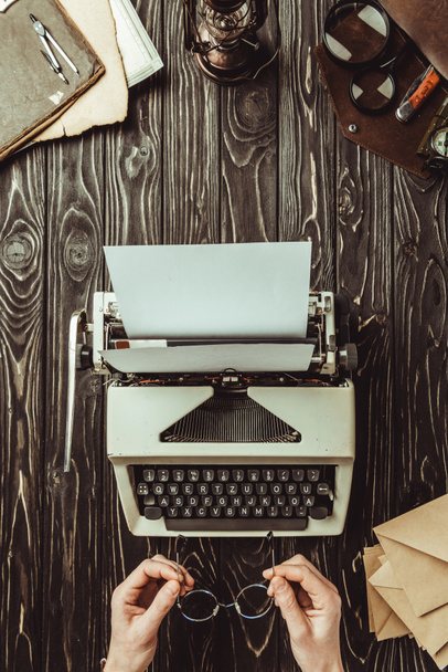 vista parcial de mujer con anteojos, máquina de escribir y sobres sobre mesa de madera
 - Foto, Imagen