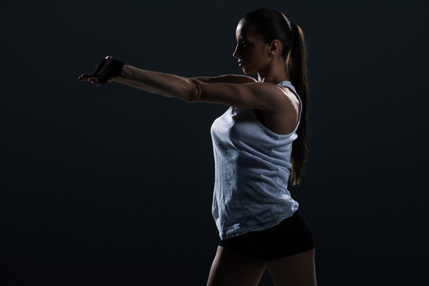 ελκυστική ισχυρή γυναίκα bodybuilder τέντωμα χέρια, απομονώνονται σε μαύρο    - Φωτογραφία, εικόνα