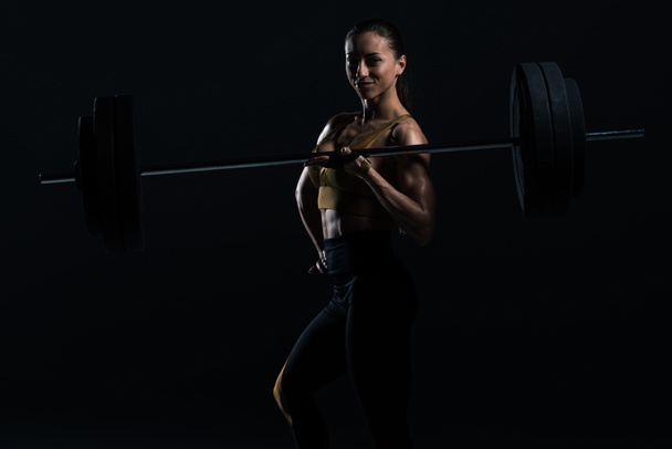 beautiful female bodybuilder posing with barbell, isolated on black    - Zdjęcie, obraz