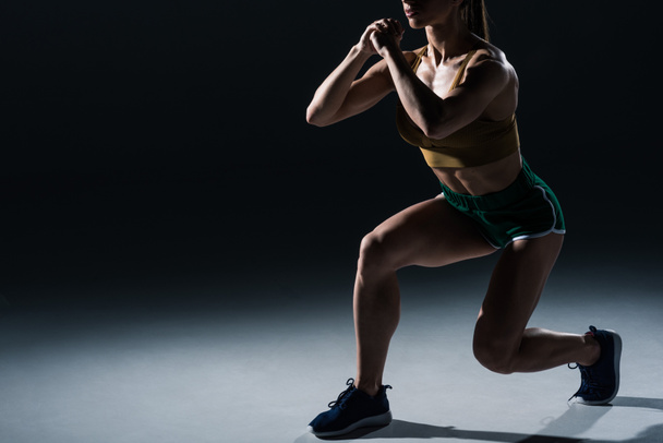 bijgesneden weergave van sportieve vrouwelijke bodybuilder doen lunges, op zwart    - Foto, afbeelding