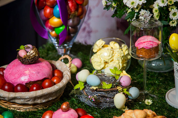 Cakes with multi-colored glaze and colorful eggs lie in wicker basket - Foto, Imagen
