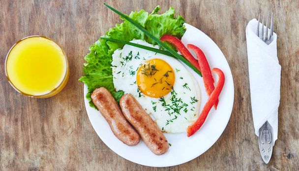 Tasty breakfast on white plate consisting from egg sausages vegatables orange juice. Top view - Photo, Image