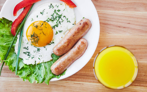 Sabroso desayuno en plato blanco que consta de huevo, salchichas vegatablesm, zumo de naranja,. Vista superior
 - Foto, Imagen