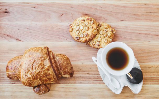 La colazione. Tazza di tè e due biscotti, croissant sul tavolo di legno. Vista dall'alto
 - Foto, immagini