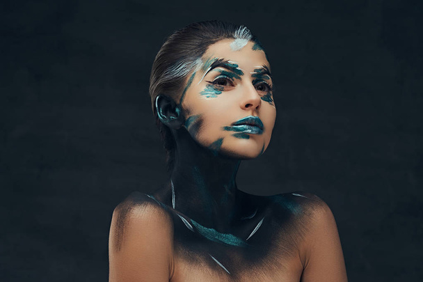 Μια αισθησιακή νεαρή κοπέλα με δημιουργικό μακιγιάζ. Μπλε και μαύρο σκιές ζωγραφισμένη στο πρόσωπό της. Εννοιολογική ιδέα. - Φωτογραφία, εικόνα