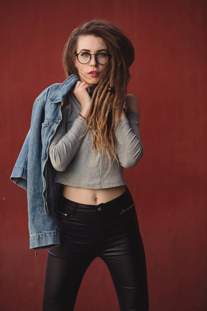 Stylish woman with dreadlocks posing against red wall background - Foto, afbeelding