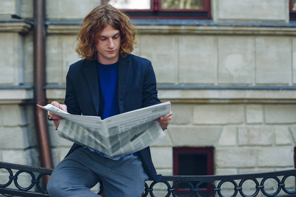 Молодий червоний чоловік читає газету біля будівлі старого стилю
 - Фото, зображення