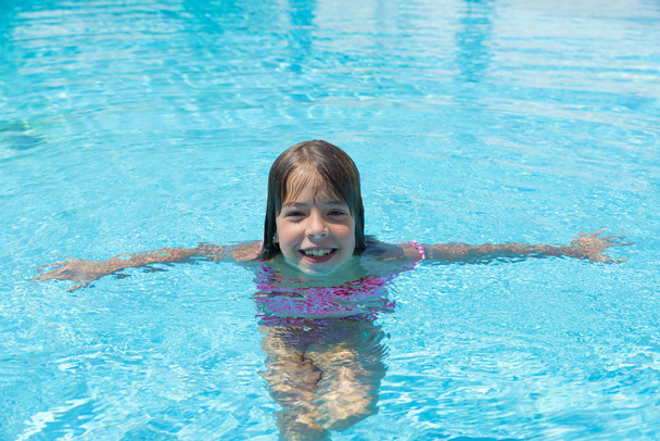Улыбающаяся маленькая девочка смотрит в камеру в открытом бассейне
 - Фото, изображение