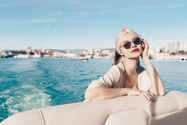 a luxurious young woman in sunglasses enjoys relaxing on her white yacht in the sun - Foto, Bild