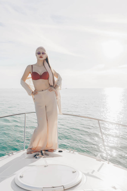 a luxurious stylish girl in sunglasses stands on her white yacht, poses, enjoys a rich life - Фото, зображення