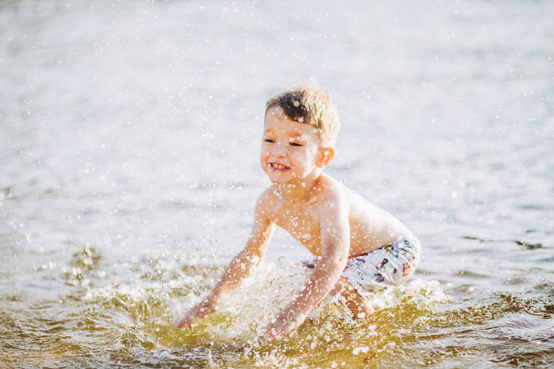 niño niño jugando hace salpicaduras, bate las manos en el agua en el río al atardecer del día
 - Foto, Imagen