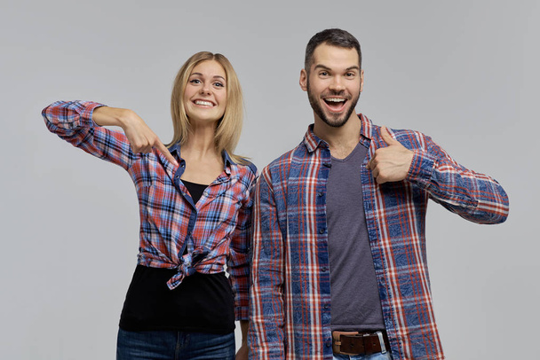 A young couple in plaid shirts and jeans - a man and a woman happily point fingers at themselves and finger up.  - Photo, image