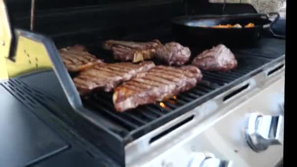 Detailní záběr rýžování klip z několika úst zalévání červené maso hovězí steaky včetně filet mignon, ribeye, a t-bone kusy značkami char na plynový gril s žluté plameny pod kovové rošty. - Záběry, video