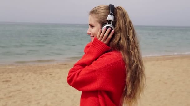 girl listens to music in large headphones on the beach by the sea - Footage, Video