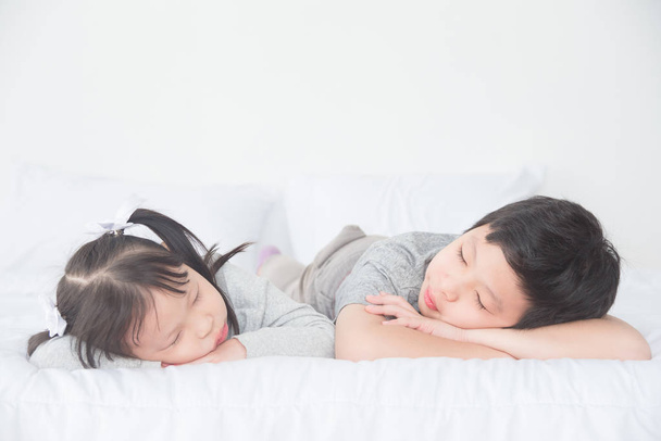 Dois irmãos asiáticos adormecem na cama durante o dia
 - Foto, Imagem