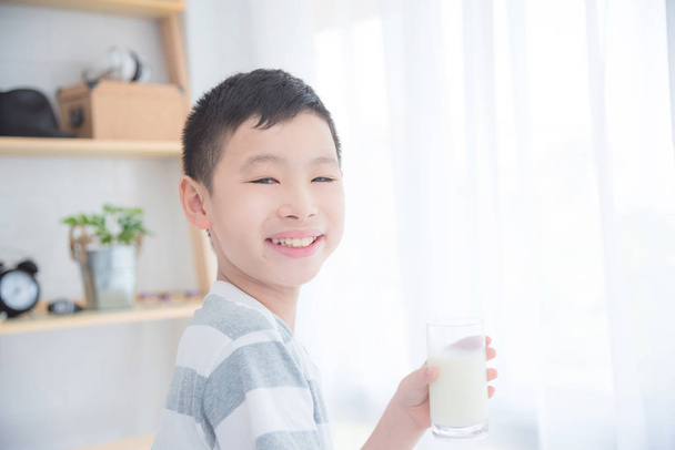 Jovem asiático menino segurando um copo de leite e sorrindo para a câmera
 - Foto, Imagem