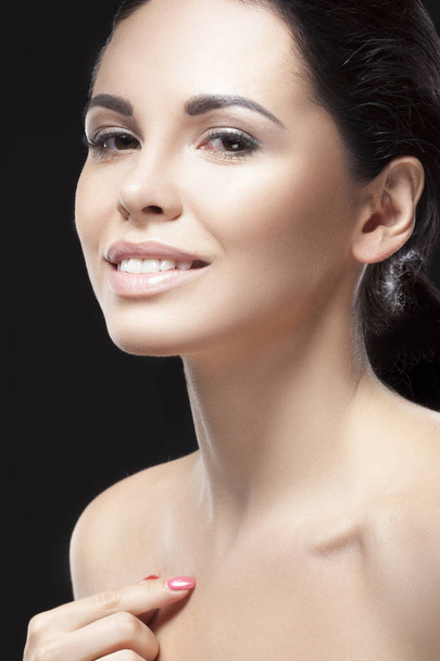 Porträt einer jungen brünetten Frau mit natürlichem Make-up und zartem Lächeln im Gesicht vor schwarzem Hintergrund - Foto, Bild