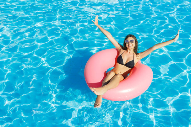 bikini girl met zonnebril ontspannen op roze opblaasbaar zwembad ring - Foto, afbeelding