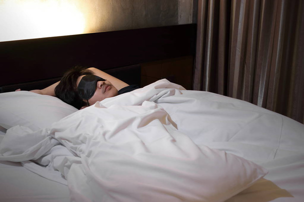 Weitwinkelaufnahme eines jungen asiatischen Mannes, der nachts bequem mit Maske auf dem Bett im Schlafzimmer schläft - Foto, Bild