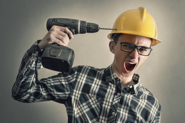 construction worker simulates shooting himself with a drill  - Foto, imagen