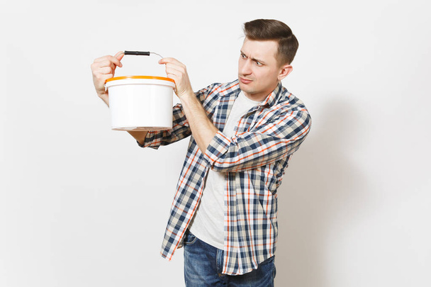Young concerned handsome man in casual clothes holding and looking on empty paint bucket with copy space isolated on white background. Instruments for renovation apartment room. Repair home concept. - Fotoğraf, Görsel
