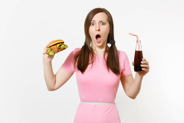Fun young woman with tails, measuring tape at waist holding burger, cola in glass bottle isolated on white background. Proper nutrition or American classic fast food. Advertising area with copy space. - Фото, изображение