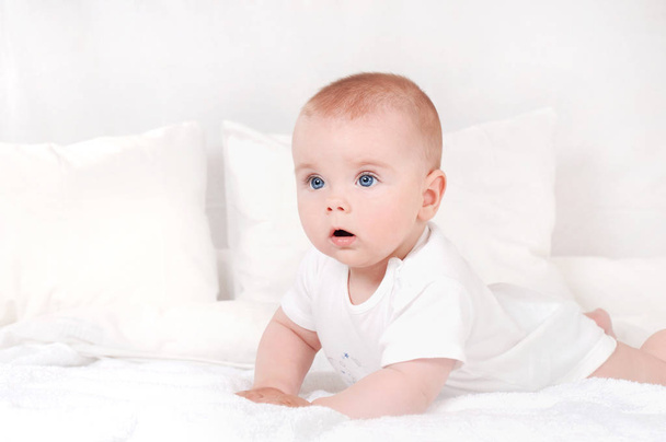 beautiful portrait of Incredible and charming small baby. Happy smiling child with blue eyes on white bed background - Φωτογραφία, εικόνα