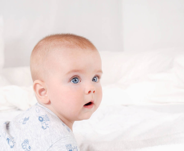 Closeup portrait of adorable newborn. Happy smiling child with blue eyes on white bed background - Fotografie, Obrázek