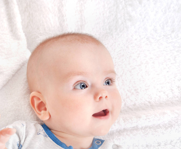 Portrait rapproché d'adorable nouveau-né. Joyeux enfant souriant aux yeux bleus sur fond de lit blanc
 - Photo, image