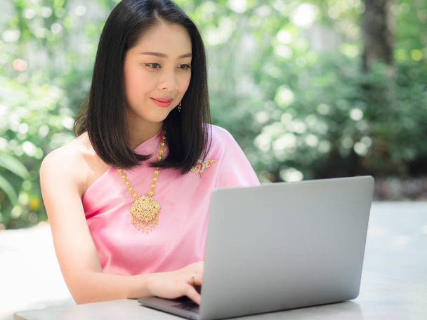 Thai woman in traditional costume is using a laptop in the garde - Photo, image