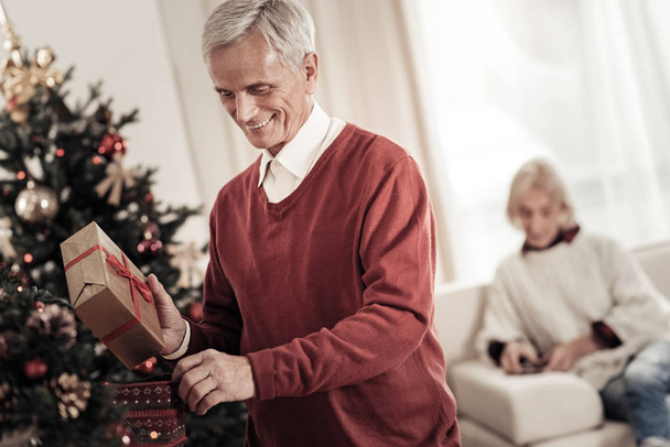 Joyful pensioner putting box into stocking - Foto, immagini