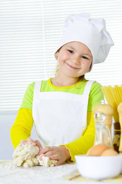 Cute little girl in chef's hat baking cake in the kitchen at home - Фото, зображення