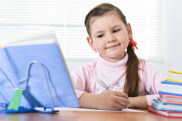 Милая школьница сидит за столом и делает домашнее задание дома
 - Фото, изображение