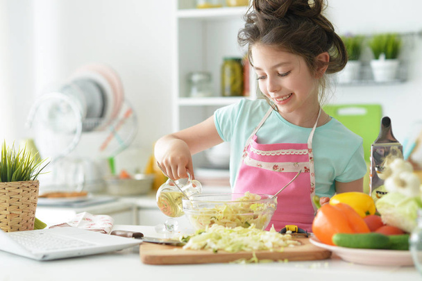 Cute girl preparing healthy salad at kitchen table with laptop  - Foto, Imagem