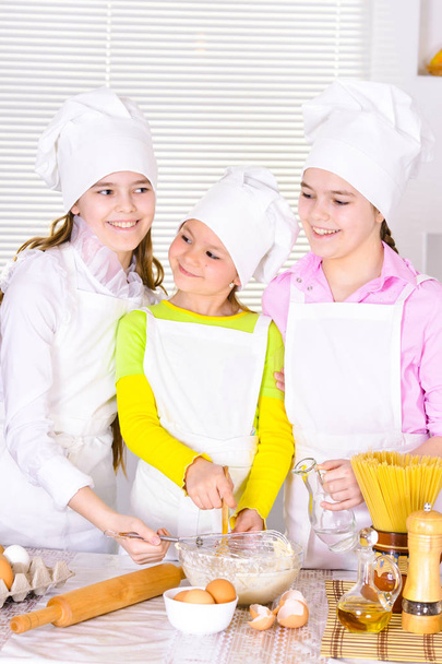 Petites filles mignonnes dans les chapeaux et tabliers du chef préparant la pâte dans la cuisine à la maison
 - Photo, image