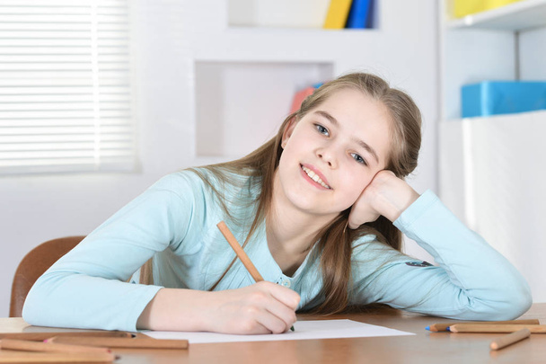 Cute schoolgirl sitting at table  and drawing - Foto, afbeelding