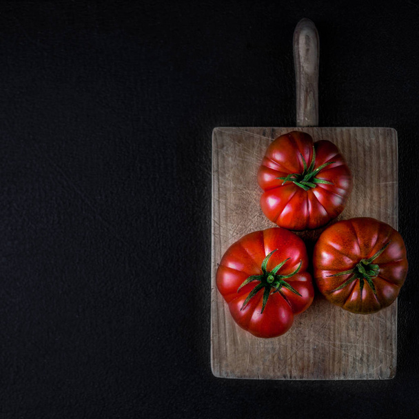Top view of raw red tomatoes on cutting board over black stone background - Foto, Bild