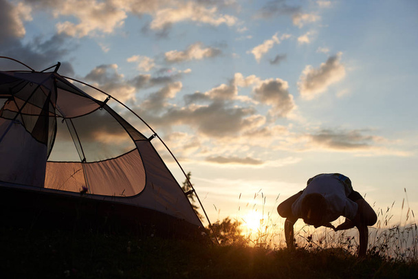 Poika harjoittelee joogaa vuoren huipulla lähellä telttaa aamun sarastaessa pilvien peitossa. Siluetti lapsen aiheuttaa jooga taustaa vasten aamutaivaan kopioi tilaa
 - Valokuva, kuva