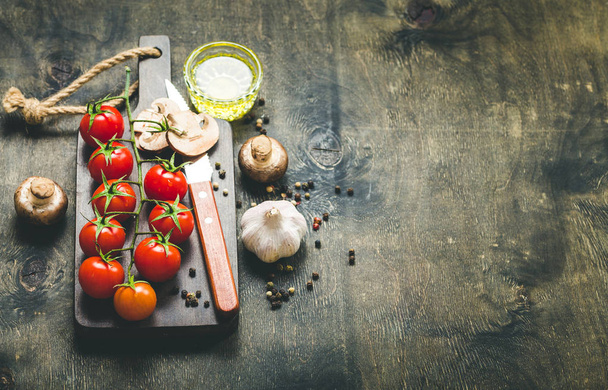 Cherry tomatoes, mushrooms on wooden cutting board, knife. With garlic, olive oil. Cooking background. Space for text. Raw ingredients for cooking. Cooking dinner. Selective focus. Food background - Photo, Image