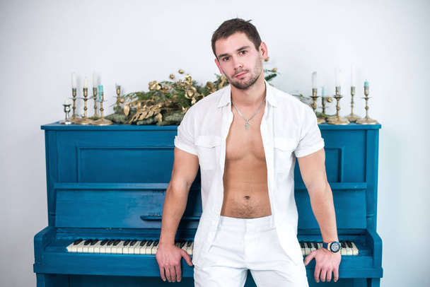 Homme réfléchi et beau avec une barbe en vêtements blancs sur le fond d'un piano, une chemise râpée avec un torse nu
 - Photo, image