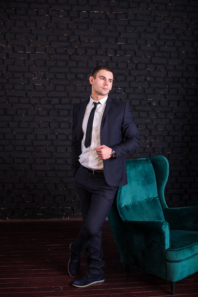 Un bell'uomo in giacca e cravatta contro un muro di mattoni neri, foto modello. Uomo di moda di successo
 - Foto, immagini
