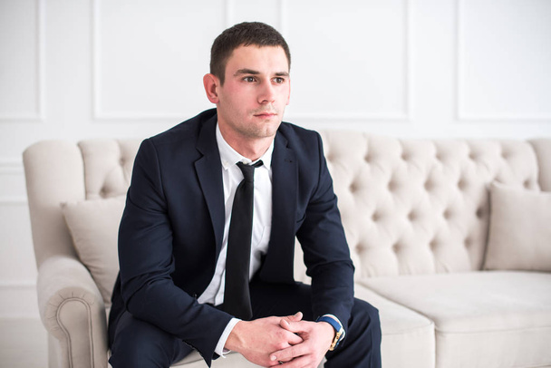 Jovem homem sério e confiante em um terno de negócios sentado no sofá
 - Foto, Imagem