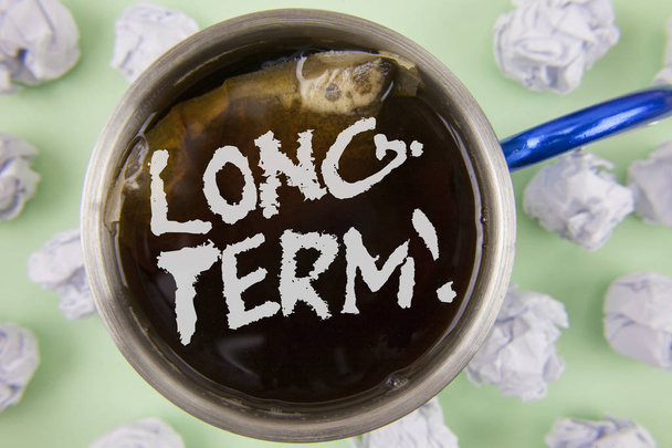 Text sign showing Long-Term Motivational Call. Conceptual photo Occurring over large period of time Future plans written on Black Tea in Cup within Crumpled Paper Balls on plain Green background. - Photo, Image