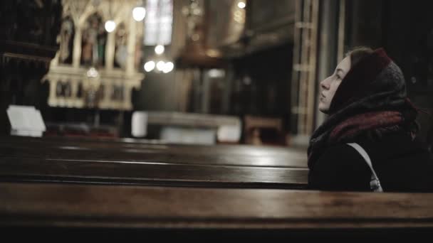 Young woman sits in catholic church. Tourist girl in cathedral: inside of holy place - Materiał filmowy, wideo