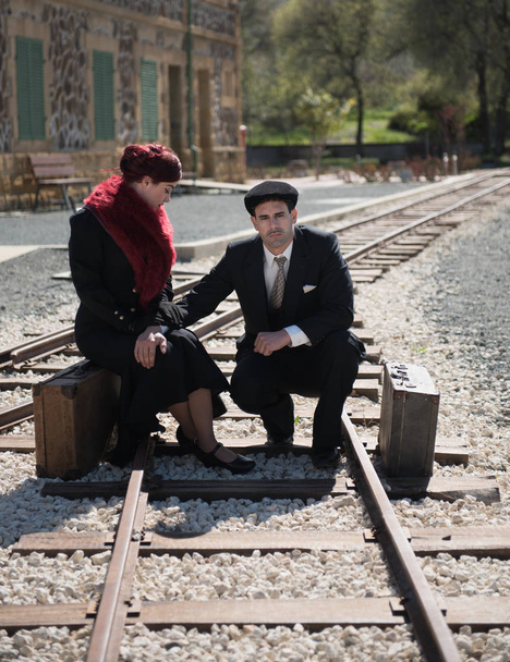 Νεαρό ζευγάρι με vintage βαλίτσα σε βαθιές σκέψεις χωροθέτηση για το trainlines που περιμένει για το επόμενο τρένο έτοιμο για το χωρισμό. - Φωτογραφία, εικόνα